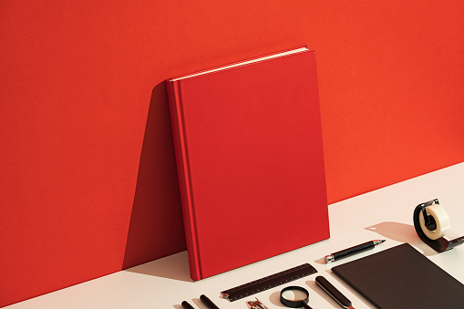 Red blank hardcover book mockup, template on red and white background. Stationary flat lay, knolling