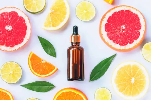 Glass bottle with cosmetic serum and sliced citrus fruits on white background. Natural cosmetics with vitamin C. Top view, flat lay.