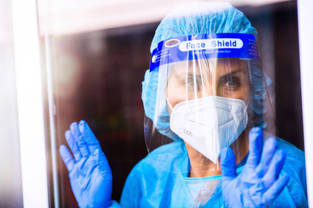istock Tired, overworked, exhausted health care worker wearing a mask and a face shield posing looking away through a window 1259267236
