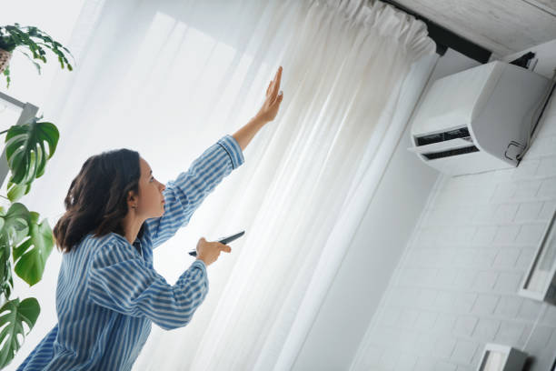 Turning on the air conditioner. Woman is checking to see if the air conditioner is cooling. She is holding the remote to the air conditioner and raised her hand to check temperature. adjusting photos stock pictures, royalty-free photos & images