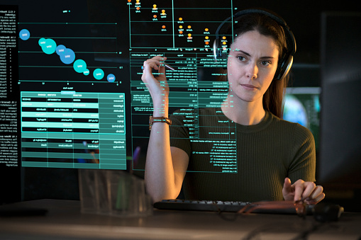 Stock photograph of a professional, good looking woman studying a see-through display showing a variety of data & information.