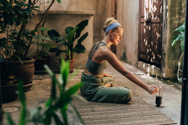 yoga no jardim: uma mulher fazendo yoga enquanto desfruta do perfume de bastões naturais de incenso - smiling serene people yoga women - fotografias e filmes do acervo