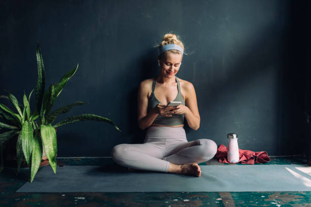istock Smiling Blonde Woman With Wireless Earphones Using her Smartphone before her Home Workout 1259290854