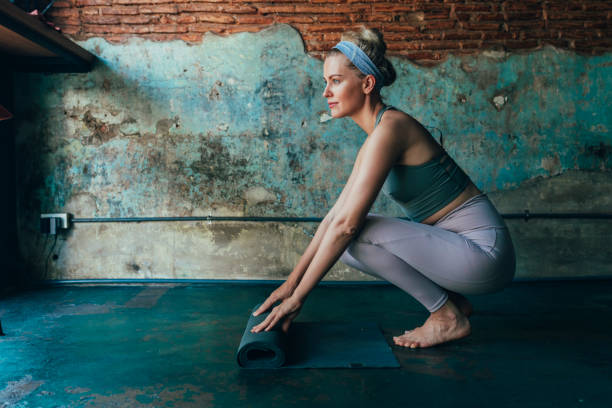 yoga a casa: donna che srotola il suo tappetino da allenamento sul pavimento (copia spazio) - unrolling foto e immagini stock