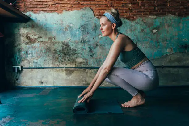 Woman in sportswear unrolling her fitness mat to do yoga at home, fitness during the lockdown concept.