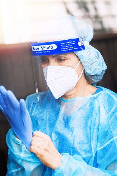 istock Tired, overworked, exhausted health care worker wearing a mask and a face shield posing looking down through a window 1259349979