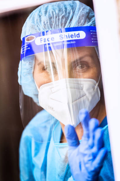 istock Tired, overworked, exhausted health care worker wearing a mask and a face shield posing looking away through a window 1259363536