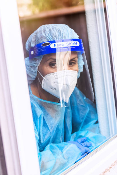 istock Tired, overworked, exhausted health care worker wearing a mask and a face shield posing looking away through a window 1259379716