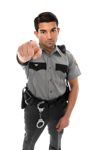 A police officer, prison guard or similar uniformed man stands firm with pointed finger.  Concept