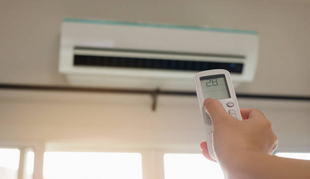 istock Hand with remote control directed on air conditioner inside the room 1259389888