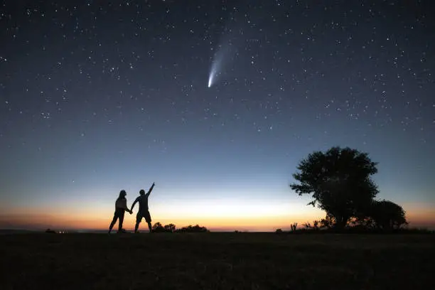 Silhouette of a young couple watching the Neowise comet under the bright night sky after sunset