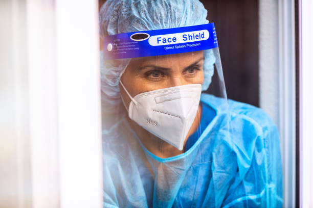 istock Tired, overworked, exhausted health care worker wearing a mask and a face shield posing looking away through a window 1259416285