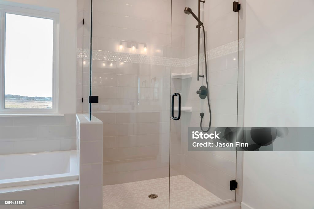 Bathroom shower stall with half glass enclosure adjacent to built in bathtub Bathroom shower stall with half glass enclosure adjacent to built in bathtub. The window offers a scenic view of snowy winter landscape and cloudy sky. Shower Stock Photo