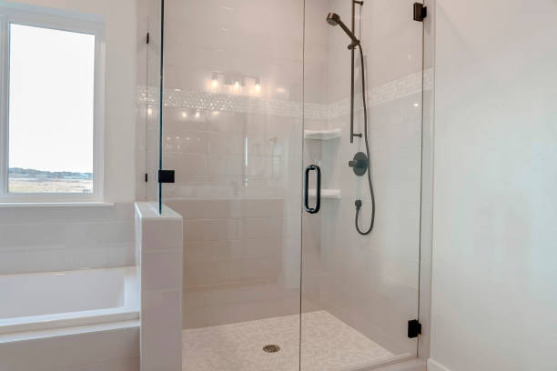 Bathroom shower stall with half glass enclosure adjacent to built in bathtub Bathroom shower stall with half glass enclosure adjacent to built in bathtub. The window offers a scenic view of snowy winter landscape and cloudy sky. enclosure stock pictures, royalty-free photos & images