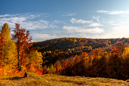 Woman looking at mountain range and colourful forest in the Laurentides area, Quebec, during sunset.