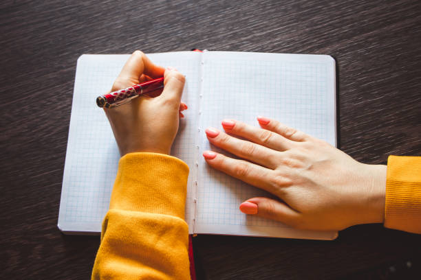 若い女性は左手にペンを持ち、白紙のノートにメモを書きます。国際左右の日 - 左利き ストックフォトと画像