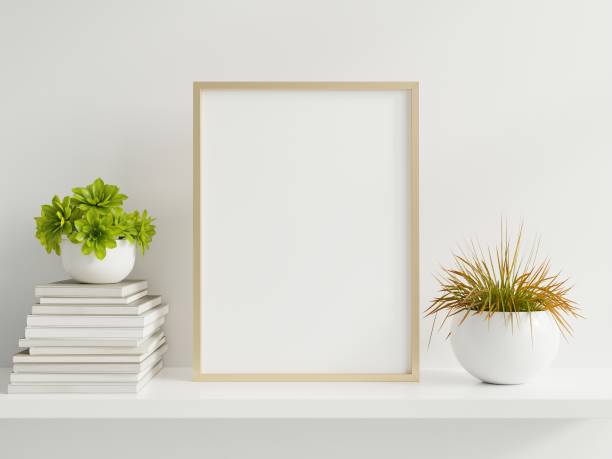 istock Wooden frame leaning on white shelf in bright interior with plants on the table with plants in pots on empty wall background. 1259505768