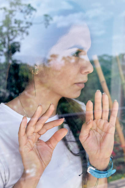 istock Lockdown Hispanic young woman looking through window 1259508396