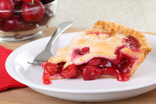 Slice of cherry pie on a plate with cherries in background