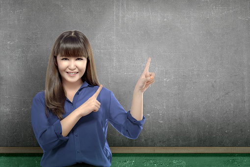 Asian student woman pointing empty chalkboard on the wall. Back to School concept. Empty chalkboard for copy space