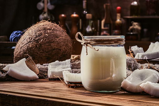Non-dairy coconut milk in glass and jar with nuts in old fashioned rustic kitchen