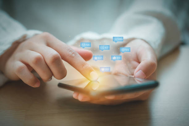 istock Asian woman using mobile phone for checking social media interactions on mobile phone with notification icons of like, love, friend, message, email, comment and star above smartphone screen. 1259581288