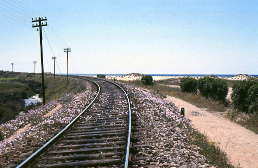 rail line disappears into distance, with telephone line beside it, red gravel pathway too