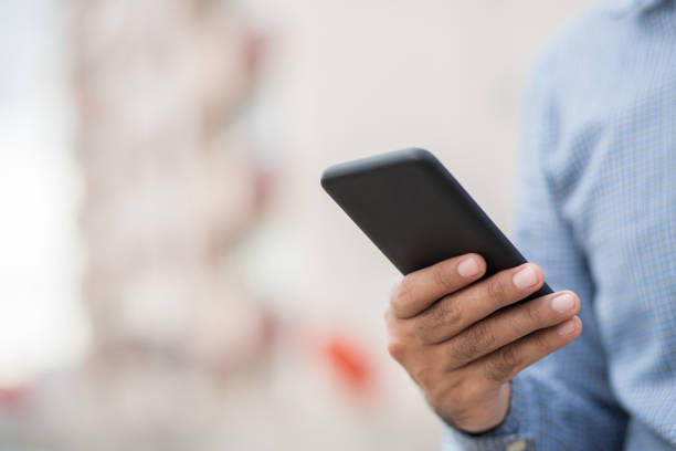 istock Close up male hands holding using black smartphone on city background. 1259607337