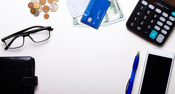 Wallet, credit card, money, glasses, blue pen, telephone and calculator lie on a light background. Business concept. Workplace close up