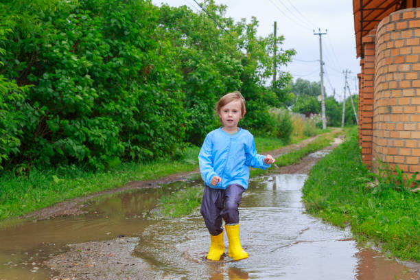 istock .Child in rubber boots and raincoat running in a puddle 1259685307