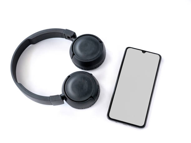 istock Black wireless headphone and mobile smartphone with a blank screen mockup lay on the surface of a white background 1259722016