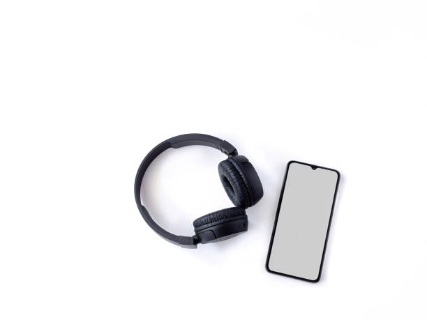istock Black wireless headphone and mobile smartphone with a blank screen mockup lay on the surface of a white background 1259722027