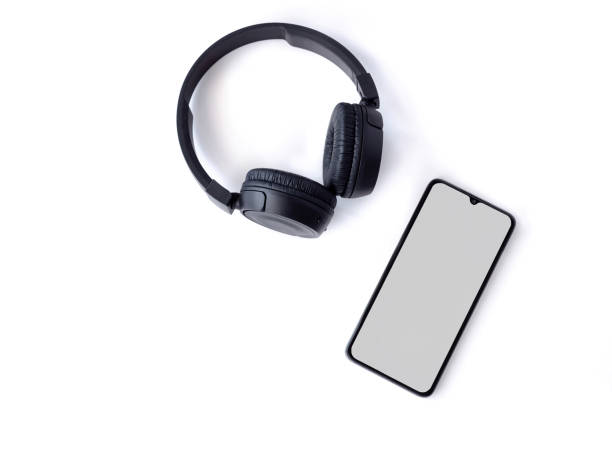 istock Black wireless headphone and mobile smartphone with a blank screen mockup lay on the surface of a white background 1259722537