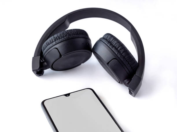istock Black wireless headphone and mobile smartphone with a blank screen mockup lay on the surface of a white background 1259722550