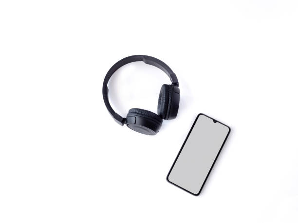 istock Black wireless headphone and mobile smartphone with a blank screen mockup lay on the surface of a white background 1259722558