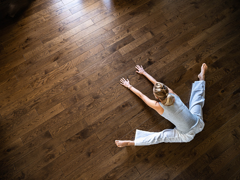 High angle view of athletic woman doing stretching exercises on a hardwood floor at home. Copy space.