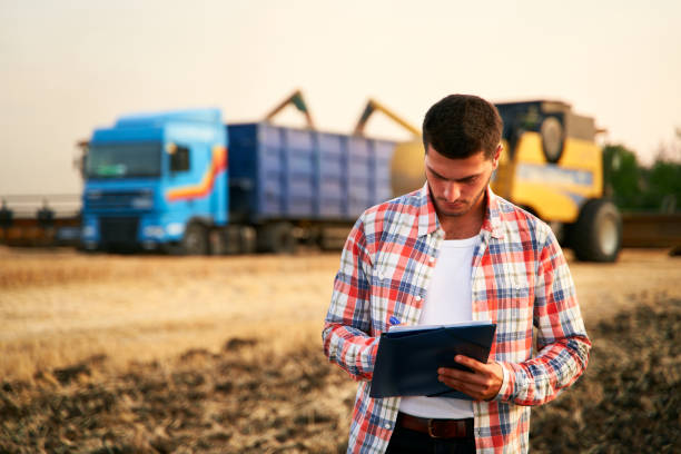 istock Farmer controls loading wheat from harvester to grain truck. Driver holding clipboard, keeping notes, cargo counting. Forwarder fills in consignment waybills. Agricultural commodities logistics 1259741744