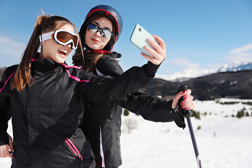 Two happy female skiers in the mountain taking selfies