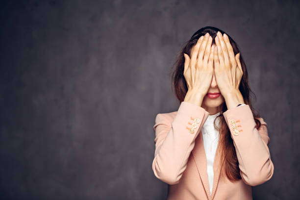 kaukasische frau, die augen auf dunklem hintergrund bedeckt - hands covering eyes stock-fotos und bilder