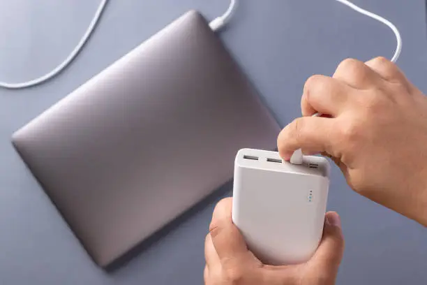 Photo of man's hands charge laptop with power bank by USB cable. Business modern technology.