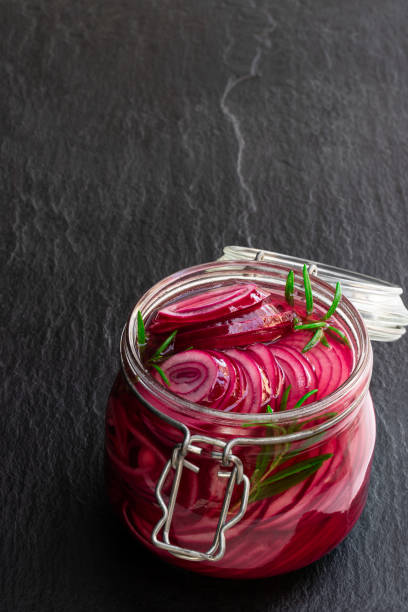 Marinated pickled red onion rings in glass jar on black stone background Marinated  pickled red onion rings in glass jar on black stone background pickled stock pictures, royalty-free photos & images