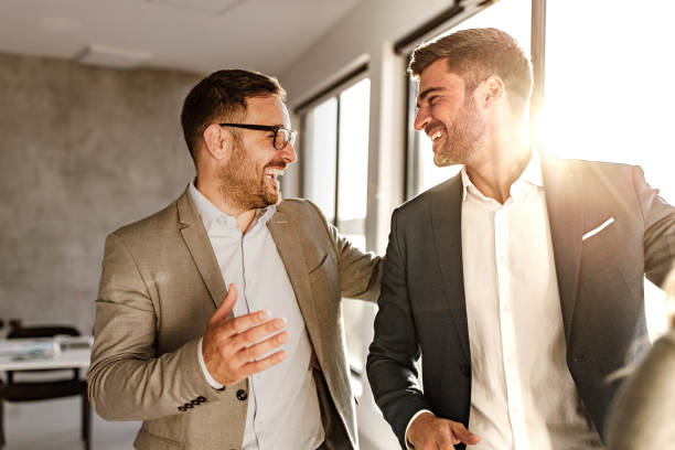 Happy businessmen talking on the move in the office. Happy male entrepreneurs communicating while walking in the office. office buddies stock pictures, royalty-free photos & images