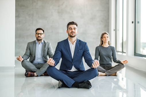 Group of business people meditating in Lotus position on the floor at casual office. Copy space.