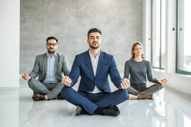 Relaxed business team exercising Yoga in the office. Group of business people meditating in Lotus position on the floor at casual office. Copy space. yoga class photos stock pictures, royalty-free photos & images