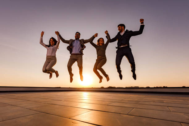 istock Playful business colleagues jumping on a rooftop at sunset. 1259861635