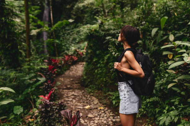 istock Traveler woman with backpack walking on path in jungle tropical deep forest, 1259875624