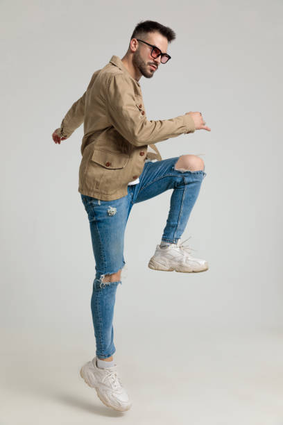 istock cool sexy young guy in jacket holding leg up and looking to side 1259897675