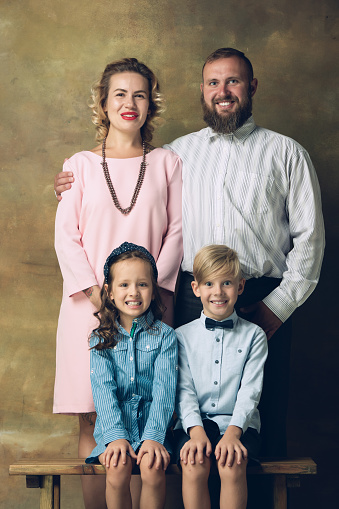 History. Happy family traditional portrait, old-fashioned. Cheerful parents and kids in official styled attire on dark vintage background. Concept of human emotions, memories, togetherness, fun.
