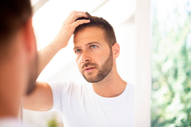 istock Handsome young man standing in front of bathroom mirror and looking his face 1259933477