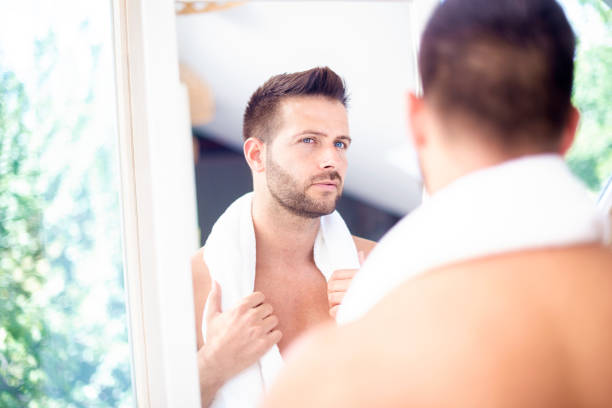 istock Handsome young man standing in front of bathroom mirror and looking his face 1259935214